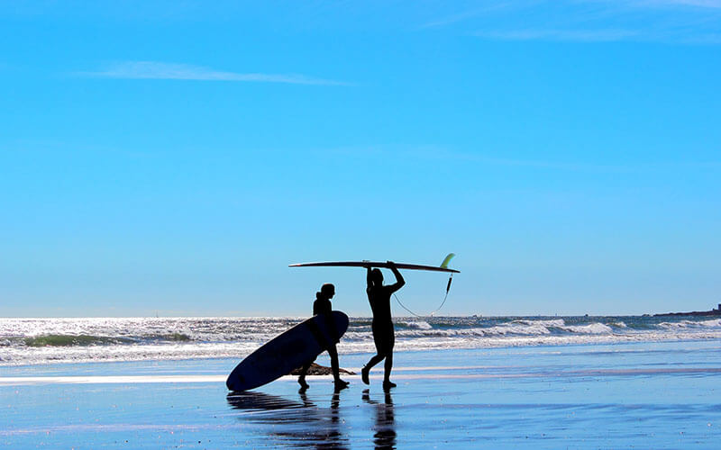0002_man-and-womans-silhouette-on-blue-background-beach-with-surf-boards-getting-ready-to-go-surfing_t20_9JVrZY